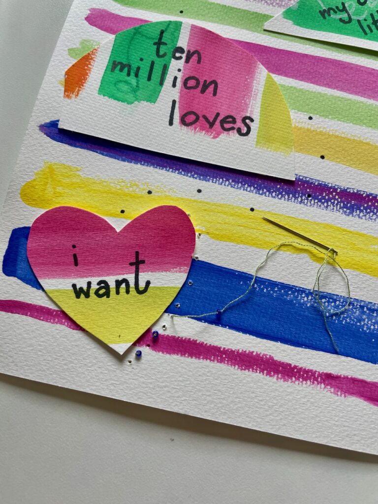 close up of art print with lyrics, embroidery needle, thread and beads