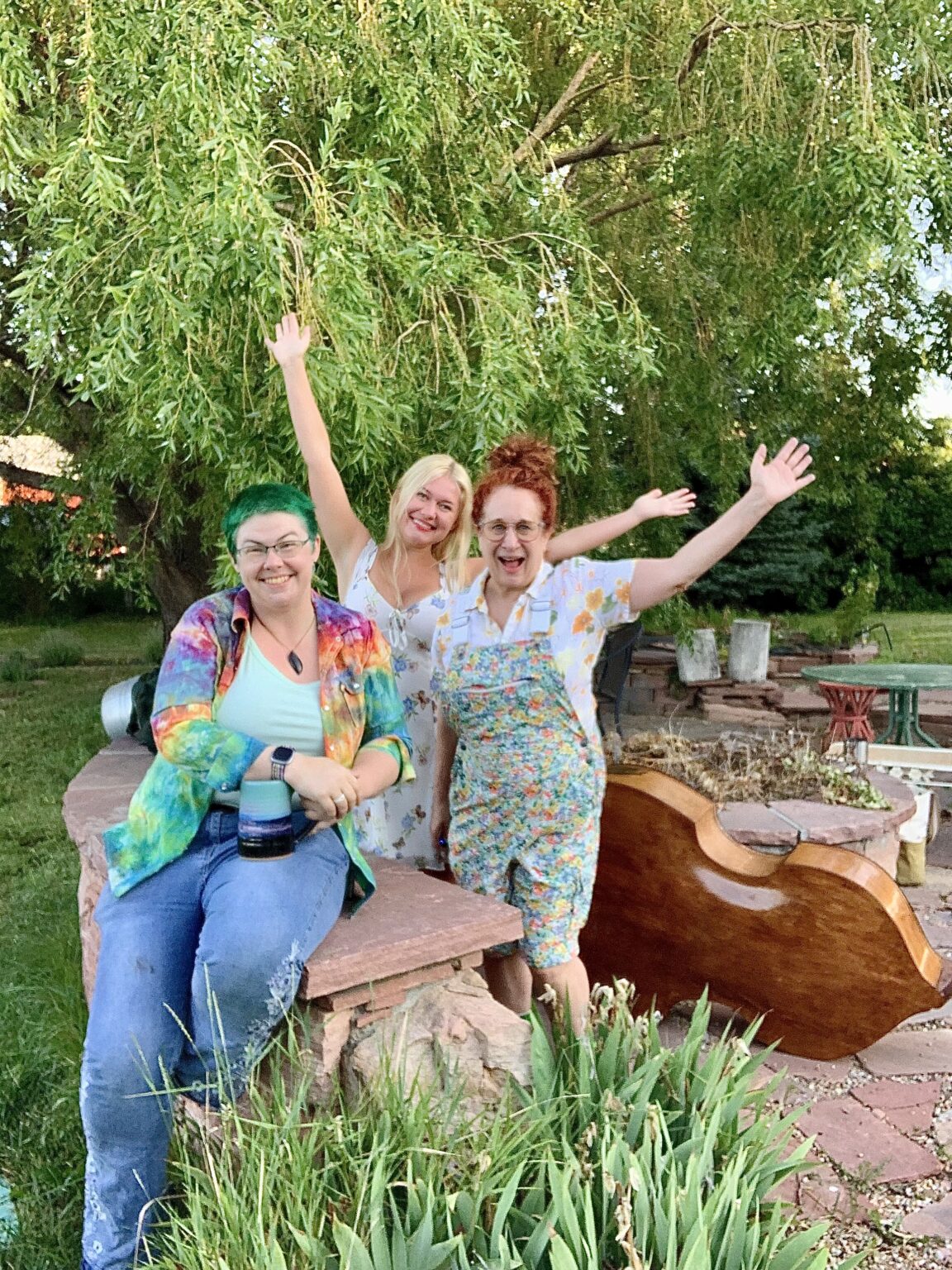 three women smiling arms outstretched under tree