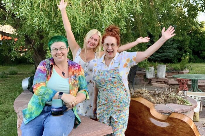three women smiling arms outstretched under tree