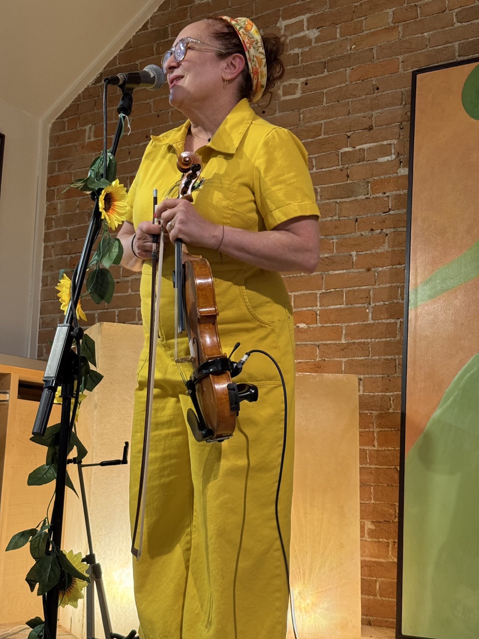 women fiddle player singing at mic stand covered in sunflowers