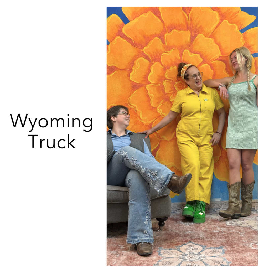 three smiling women sitting and chatting against flower mural Wyoming Truck typography