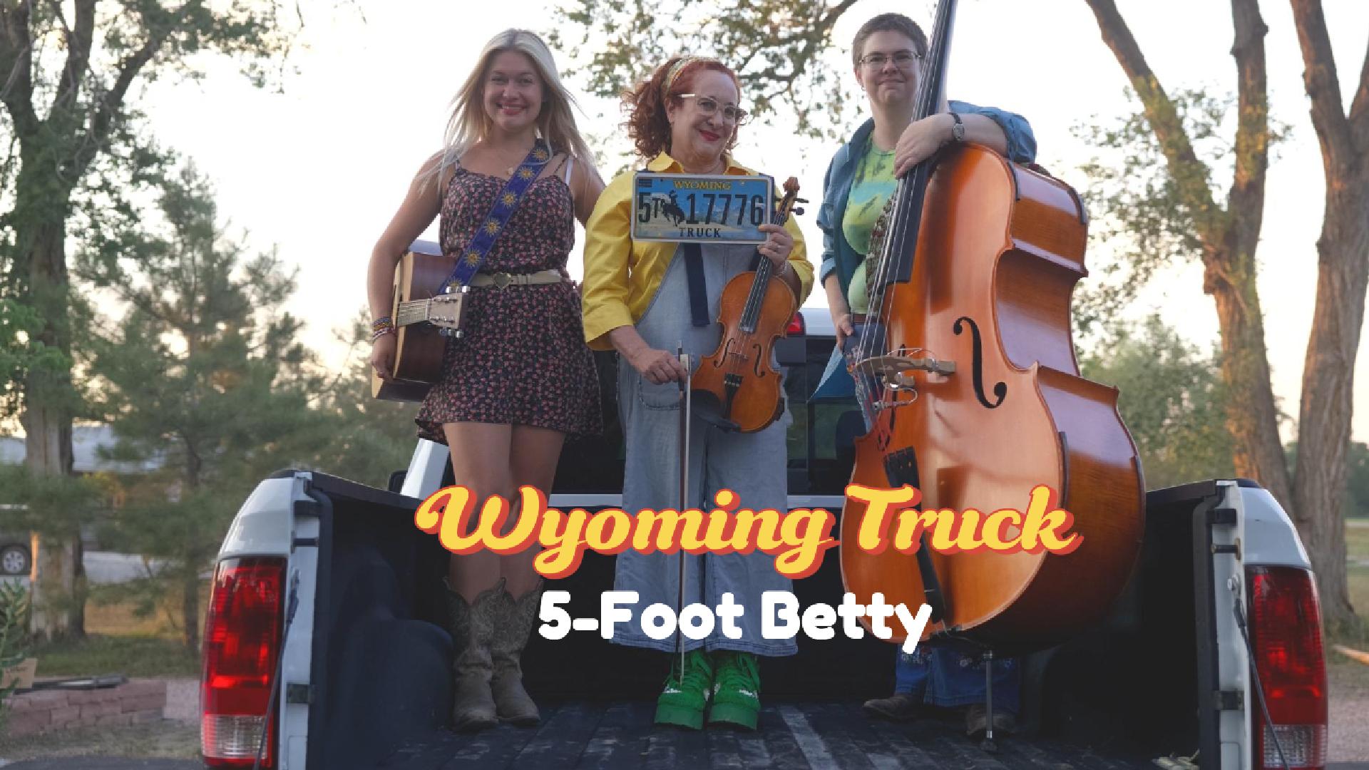 three smiling women with instrument standing in flatbed truck