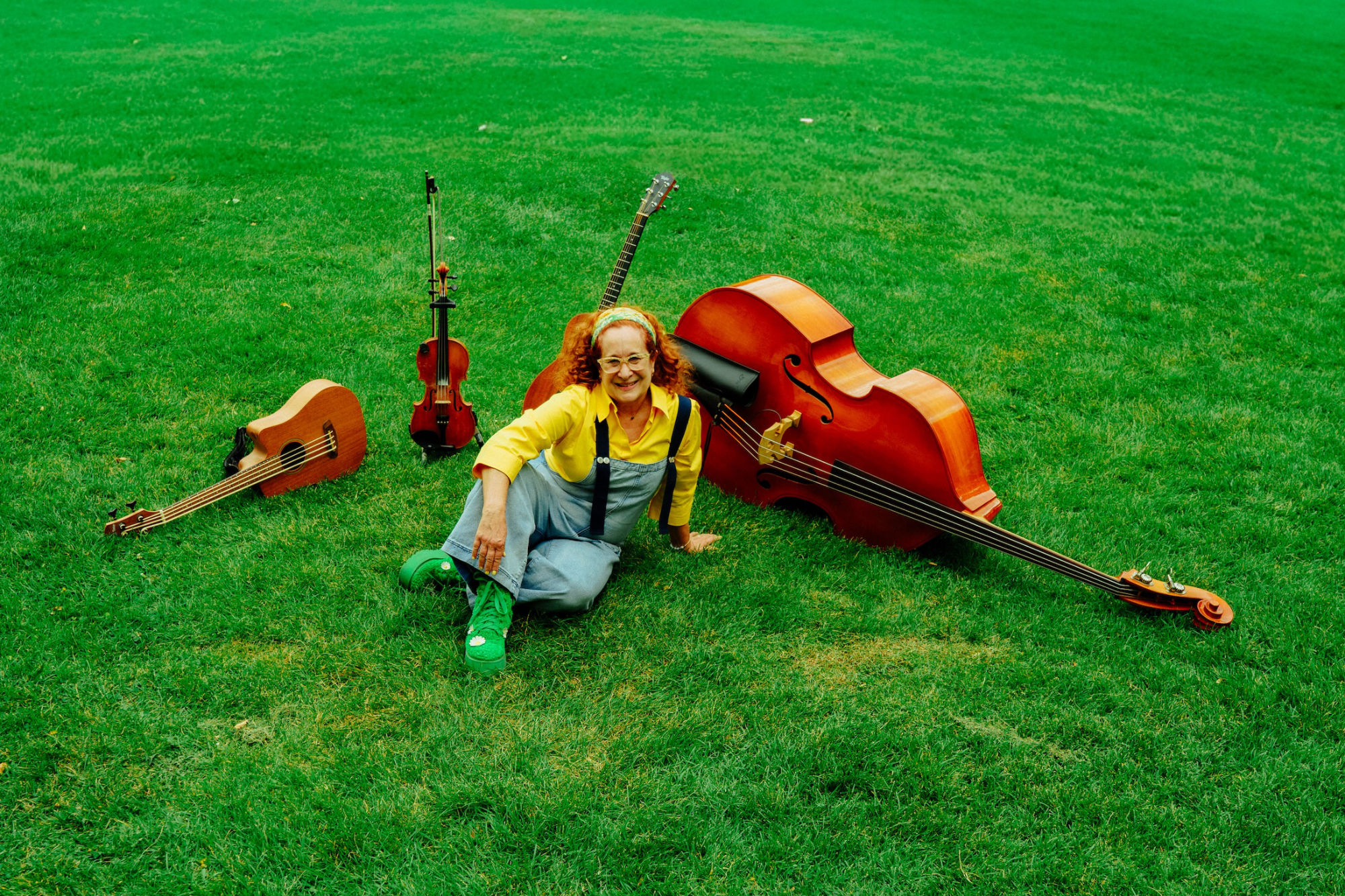 woman in overalls sitting on green lawn surrounded by fiddle, upright bass, guitar and mandolin