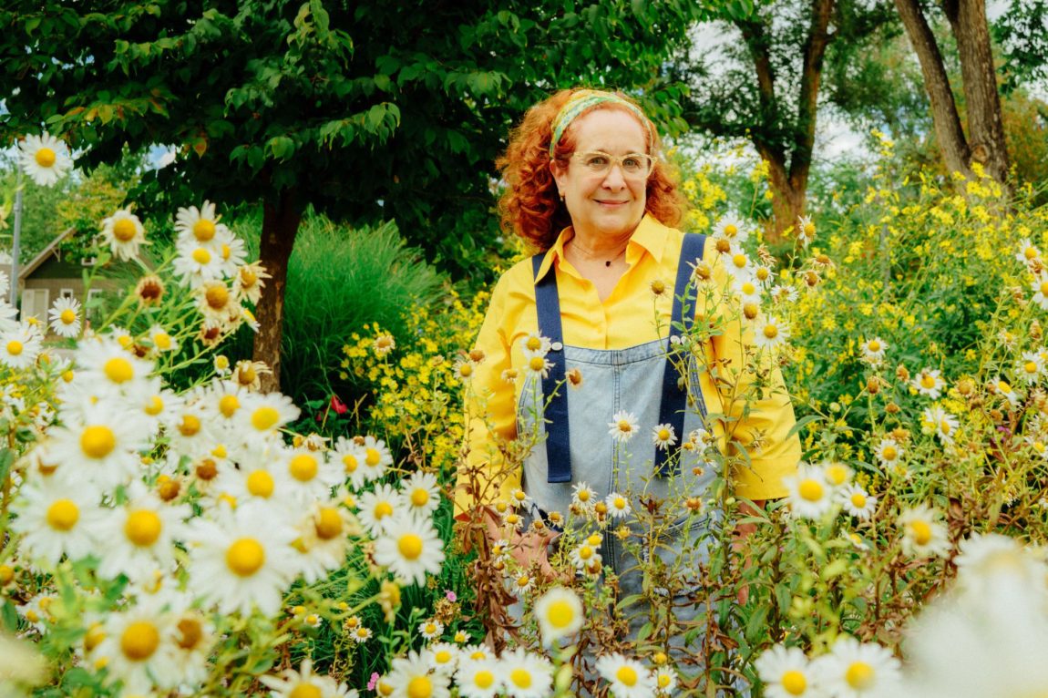 red haired woman in overalls standing in field of daises